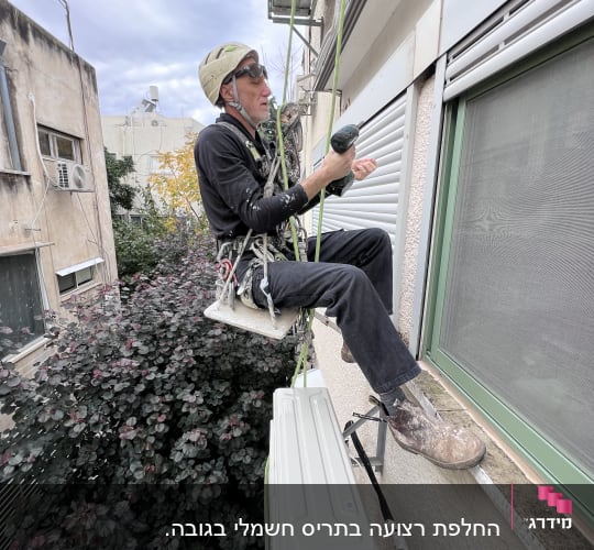 אדם מתקין תריסים חיצוניים על קיר בניין